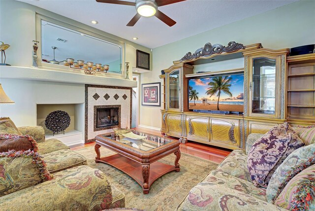 living room featuring ceiling fan, a tile fireplace, and light hardwood / wood-style flooring