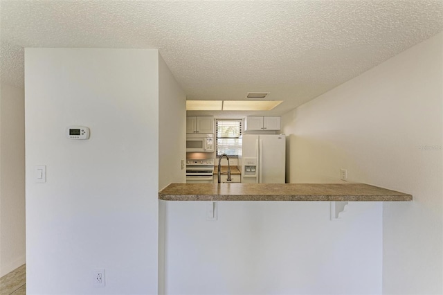 kitchen with white appliances, a textured ceiling, sink, and a breakfast bar