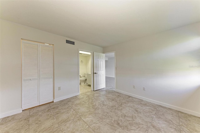 unfurnished bedroom featuring light tile floors, connected bathroom, and a closet