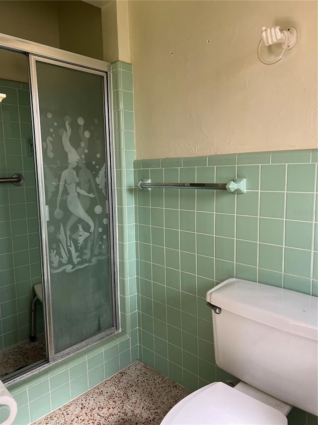 bathroom featuring toilet, a shower with door, and tile walls