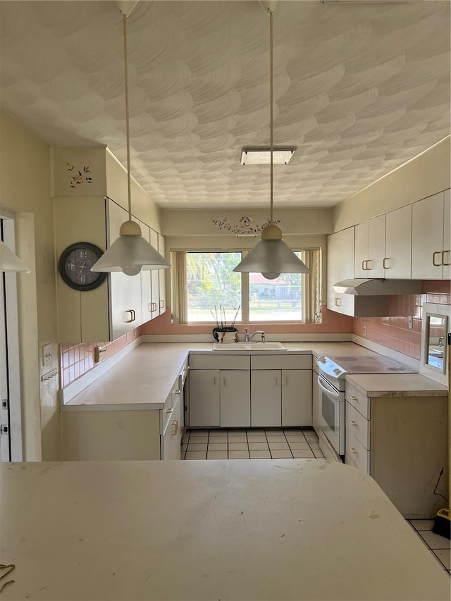 kitchen featuring white range with electric stovetop, decorative light fixtures, light tile flooring, white cabinets, and backsplash