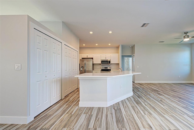 kitchen featuring ceiling fan, sink, an island with sink, stainless steel appliances, and white cabinets