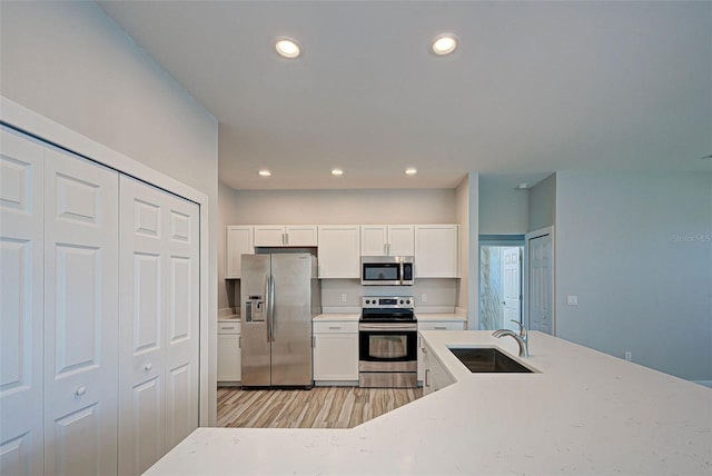 kitchen with sink, white cabinets, appliances with stainless steel finishes, light stone countertops, and light wood-type flooring