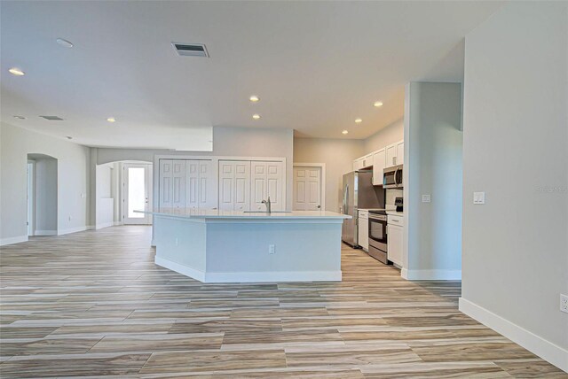 kitchen with sink, white cabinets, appliances with stainless steel finishes, a center island with sink, and light hardwood / wood-style floors