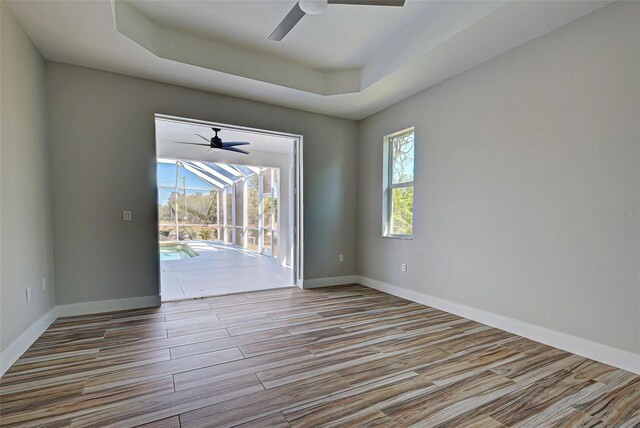 empty room featuring a raised ceiling, ceiling fan, and a wealth of natural light