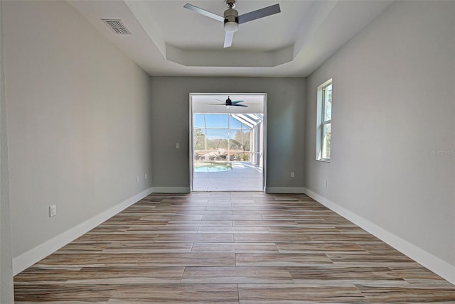 empty room featuring a healthy amount of sunlight, ceiling fan, and a tray ceiling