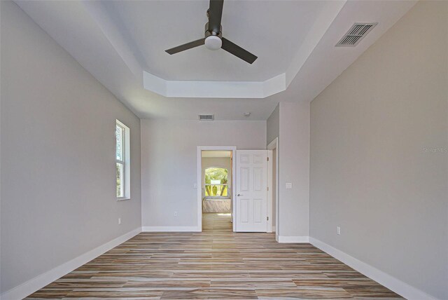 unfurnished room with light hardwood / wood-style floors, a tray ceiling, and ceiling fan