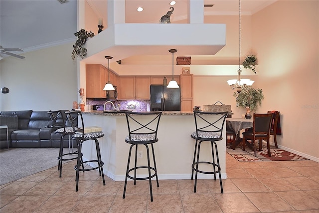 kitchen featuring a towering ceiling, ceiling fan with notable chandelier, black fridge, and light tile flooring