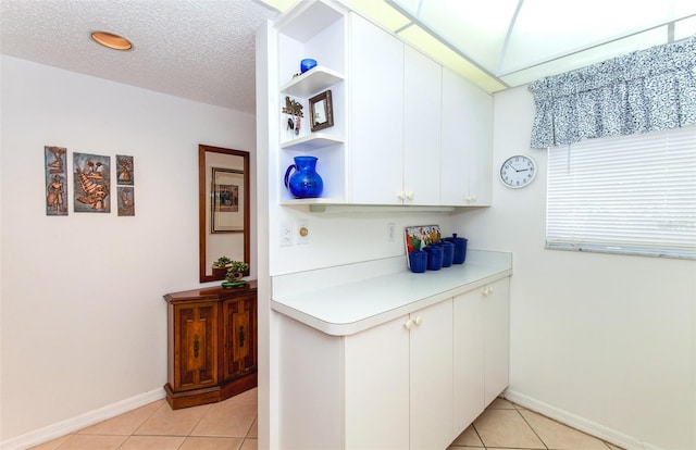 kitchen with a textured ceiling, light tile floors, and white cabinetry