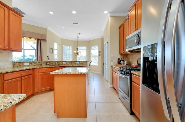 kitchen with stainless steel appliances, a kitchen island, hanging light fixtures, and light stone counters