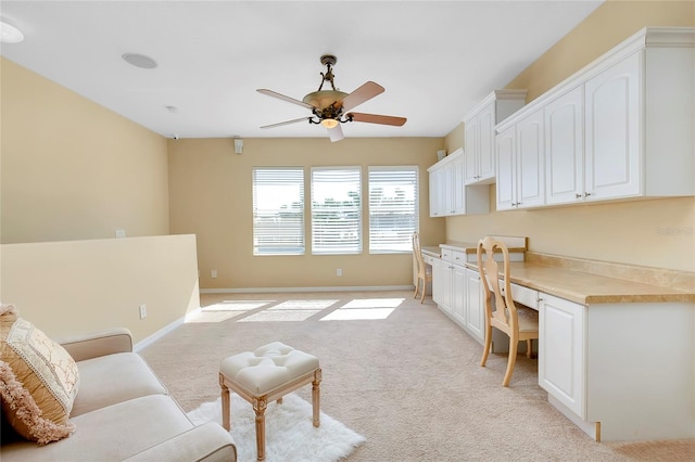 office area with built in desk, light colored carpet, and ceiling fan