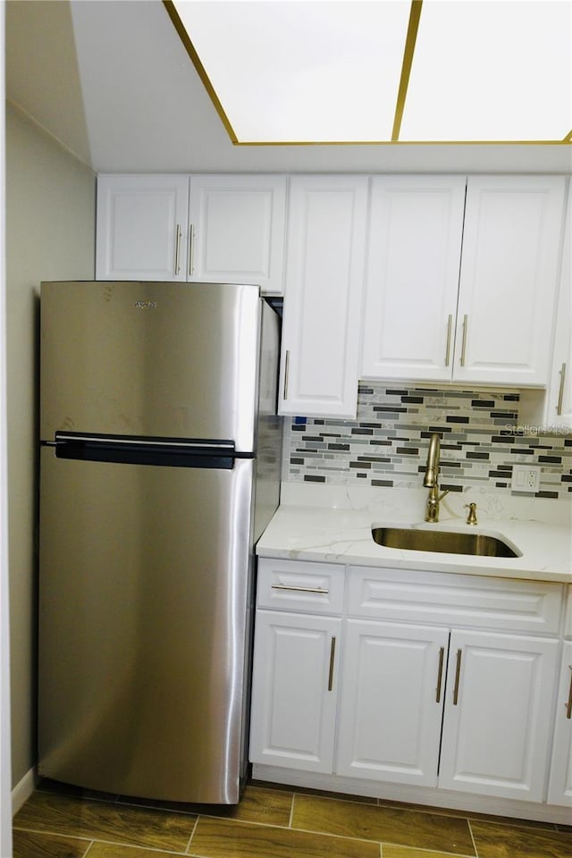 kitchen featuring sink, decorative backsplash, white cabinets, dark wood-type flooring, and stainless steel refrigerator