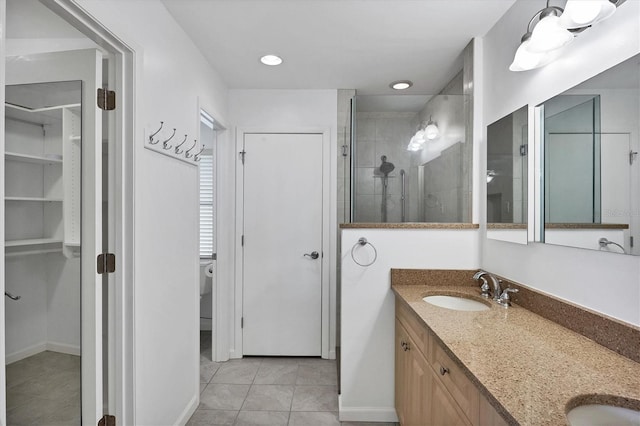 full bath featuring a tile shower, double vanity, a sink, and a walk in closet