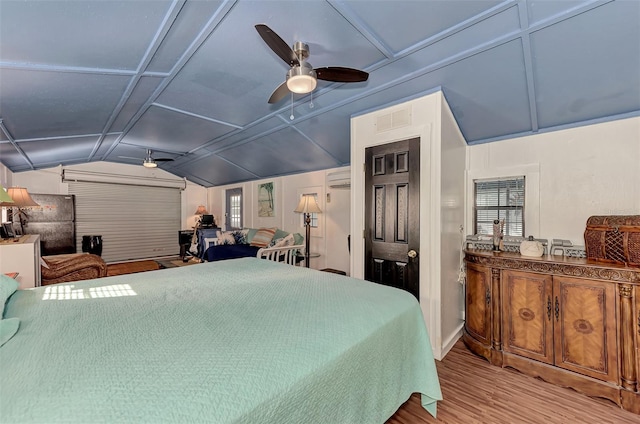 bedroom featuring wood finished floors, visible vents, freestanding refrigerator, vaulted ceiling, and an AC wall unit