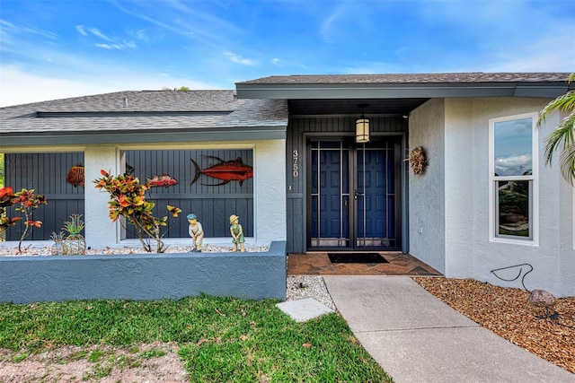 view of exterior entry with stucco siding and roof with shingles