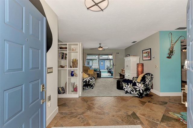 foyer entrance featuring stone finish flooring, baseboards, visible vents, and ceiling fan