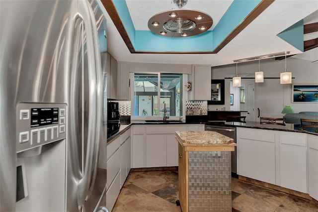 kitchen featuring a tray ceiling, a sink, stainless steel fridge, white cabinets, and tasteful backsplash