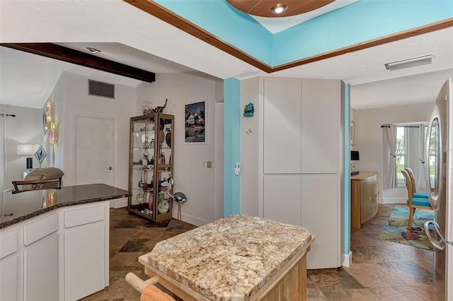 kitchen with dark stone countertops, stone tile floors, visible vents, and freestanding refrigerator