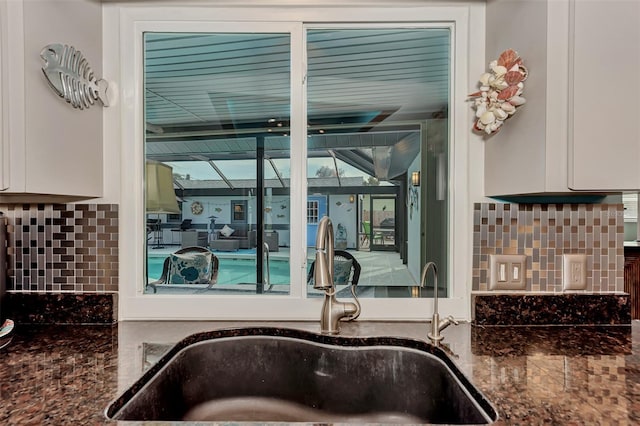 details featuring dark stone countertops, tasteful backsplash, sink, and white cabinets