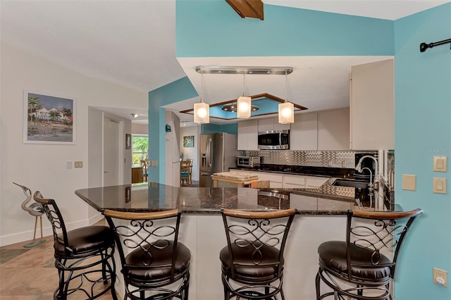 kitchen with a peninsula, a sink, vaulted ceiling, appliances with stainless steel finishes, and backsplash