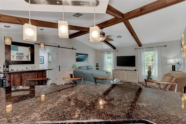 kitchen with a barn door, vaulted ceiling with beams, visible vents, and a wealth of natural light