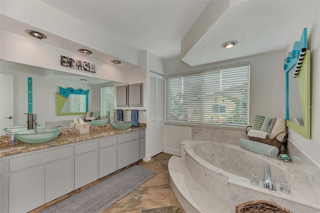 full bath with double vanity, baseboards, a garden tub, and a sink