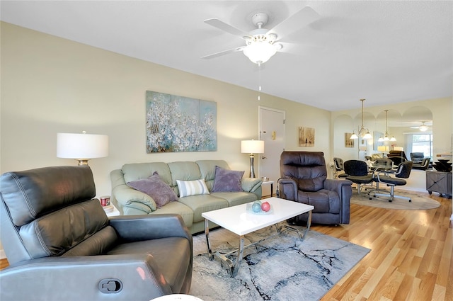 living room featuring ceiling fan with notable chandelier and light wood-type flooring