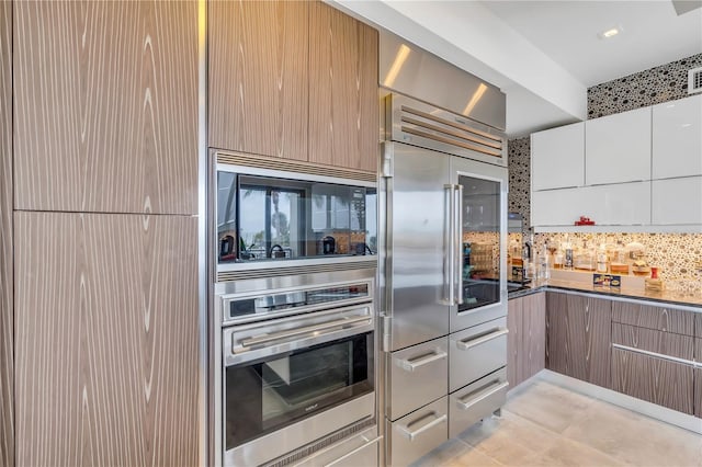 kitchen featuring tasteful backsplash, white cabinetry, and built in appliances