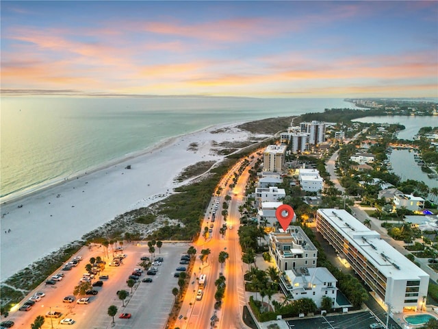 aerial view at dusk featuring a view of the beach and a water view