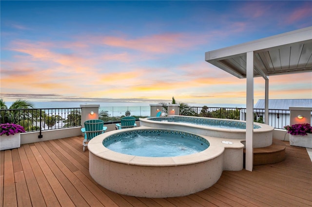 pool at dusk featuring a water view and an outdoor hot tub