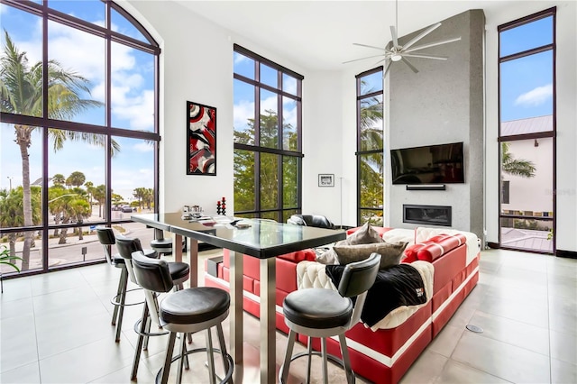 interior space featuring a towering ceiling, a fireplace, ceiling fan, and a wall of windows