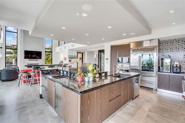 kitchen with sink, built in appliances, dark stone counters, and a spacious island