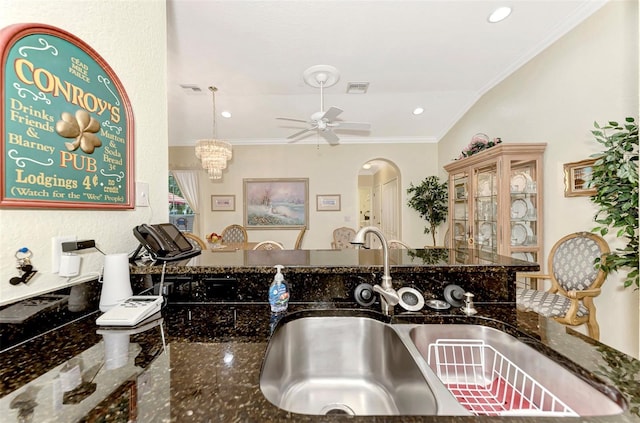 kitchen with dark stone counters, ceiling fan with notable chandelier, ornamental molding, hanging light fixtures, and sink