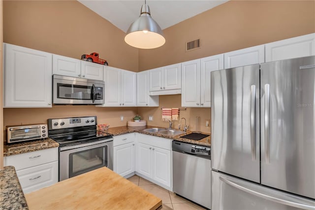 kitchen with hanging light fixtures, appliances with stainless steel finishes, light tile floors, white cabinets, and dark stone counters