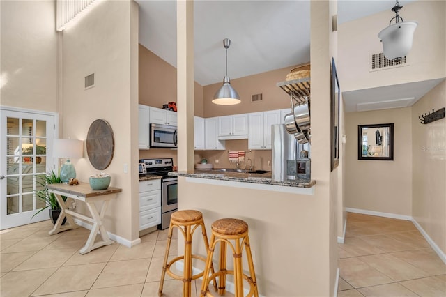 kitchen with high vaulted ceiling, stainless steel appliances, white cabinets, and dark stone counters