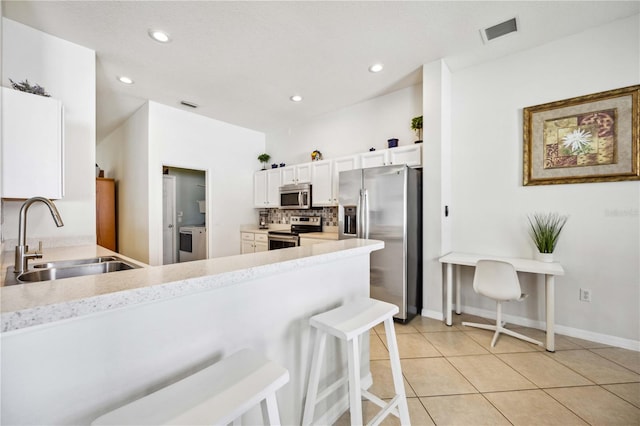 kitchen featuring sink, white cabinets, backsplash, stainless steel appliances, and a kitchen bar