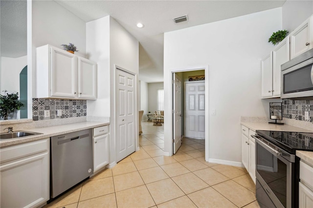 kitchen featuring light tile flooring, light stone countertops, appliances with stainless steel finishes, white cabinets, and backsplash