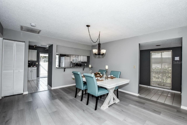 dining room with hardwood / wood-style flooring, a chandelier, sink, and a textured ceiling