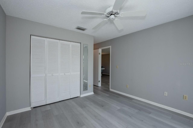 unfurnished bedroom featuring ceiling fan, a textured ceiling, light wood-type flooring, and a closet