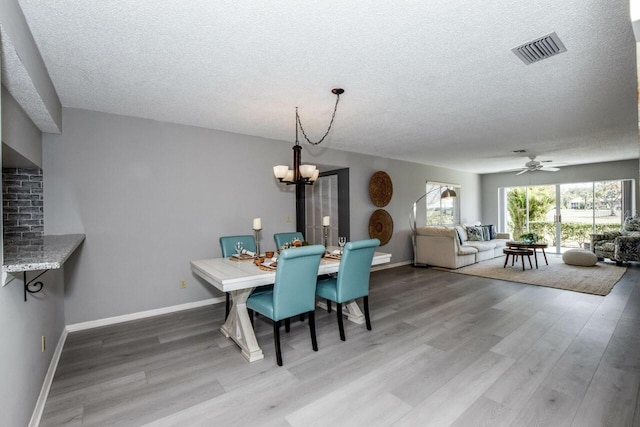 dining area featuring hardwood / wood-style flooring, ceiling fan with notable chandelier, and a textured ceiling