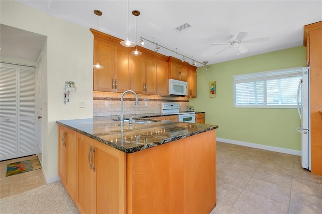 kitchen featuring sink, kitchen peninsula, pendant lighting, white appliances, and dark stone counters