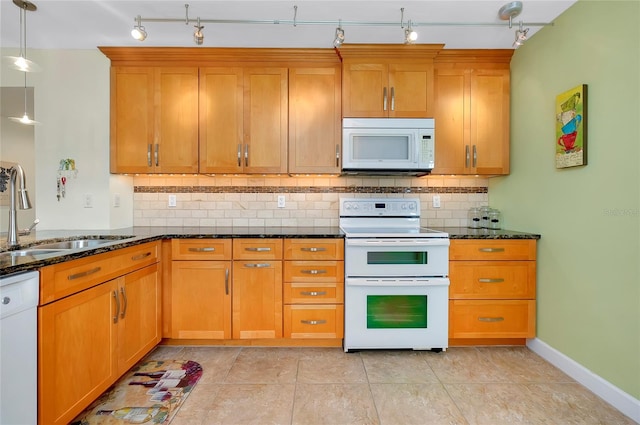 kitchen featuring pendant lighting, tasteful backsplash, sink, dark stone countertops, and white appliances