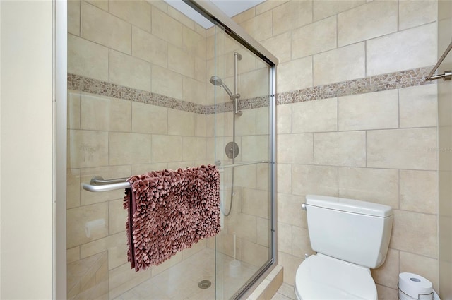 bathroom featuring a shower with door and toilet