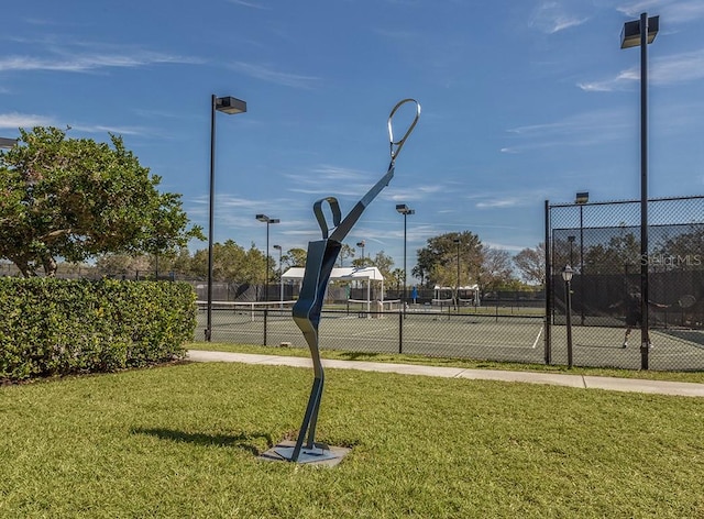 view of tennis court with fence and a lawn