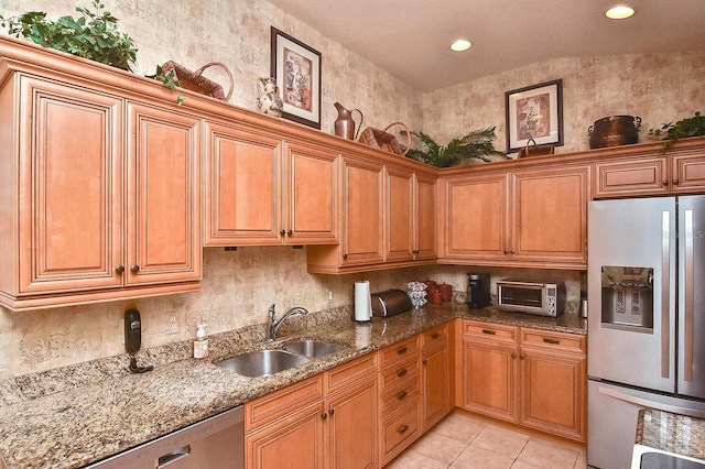 kitchen with sink, stainless steel appliances, dark stone countertops, light tile floors, and vaulted ceiling