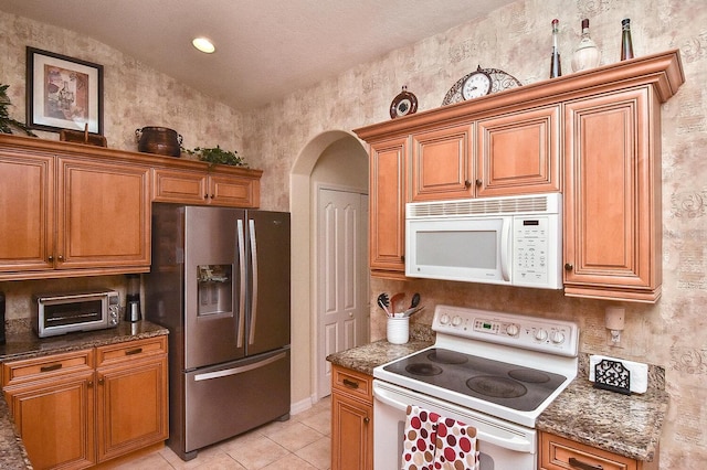 kitchen with vaulted ceiling, white appliances, dark stone countertops, and light tile flooring