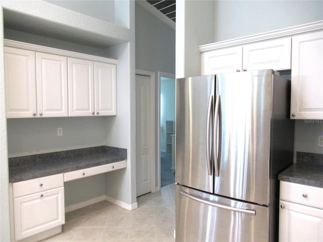 kitchen featuring built in desk, stainless steel refrigerator, and white cabinetry