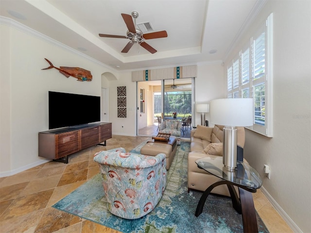 living room featuring a raised ceiling, crown molding, light tile flooring, and ceiling fan