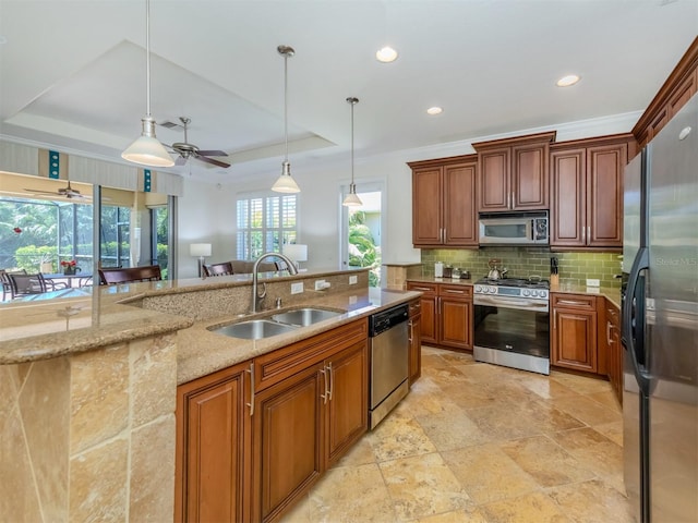 kitchen with pendant lighting, ceiling fan, sink, appliances with stainless steel finishes, and a tray ceiling