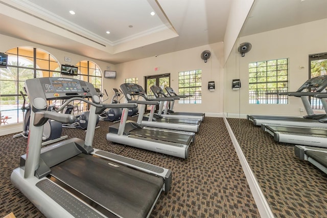 workout area with dark carpet, a tray ceiling, and a wealth of natural light